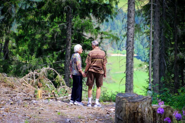 Elderly couple holding hands and walking through a peaceful forest, surrounded by greenery and nature.